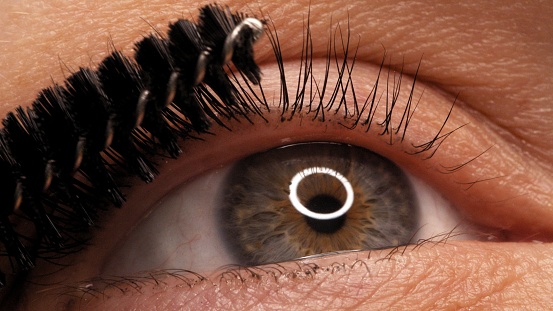 Making makeup in a beauty salon. Applying black mascara to the eyelashes with a makeup brush. Close-up of a woman's eye. Lengthening of the eyelashes after lamination.