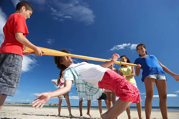 Teenagers doing limbo dance on beach having fun