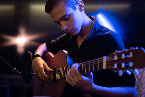 Man with a classical guitar in a neon glow. Teenager plays guitar.  Young man plays a musical instrument.