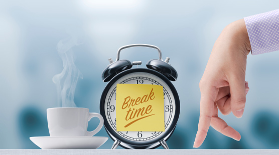 Walking fingers going towards a cup of coffee and alarm clock with sticky note, it's break time
