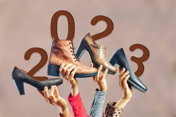 mani che tengono diverse scarpe e stivali da donna con l'anno 2023 su di loro. concetto di capodanno - vogue 40th foto e immagini stock