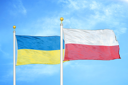 Poland and Ukraine two flags on flagpoles blue sky background