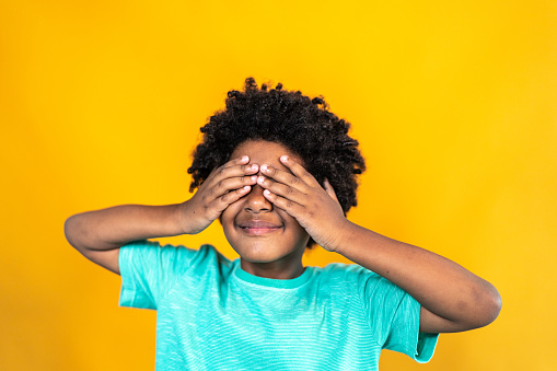 Boy covering eyes with hands on a yellow background