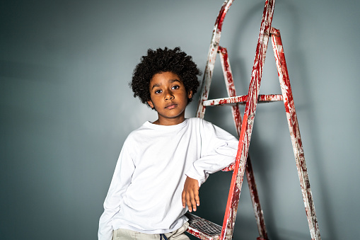 Portrait of a boy leaning on a ladder on a gray background