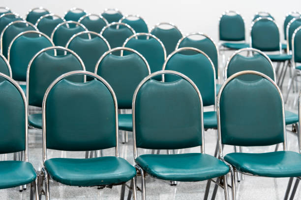 istock Many empty green leather chairs in a wide hall room, lights on. A floor reflect the objects. Give a feeling of emptiness. 1423988122