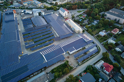 Aerial view of solar power plant with blue photovoltaic panels mounted on industrial building roof for producing green ecological electricity. Production of sustainable energy concept.