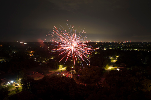 Aerial view of bright fireworks exploding with colorful lights over suburban houses in residential area on US Independence day holiday.