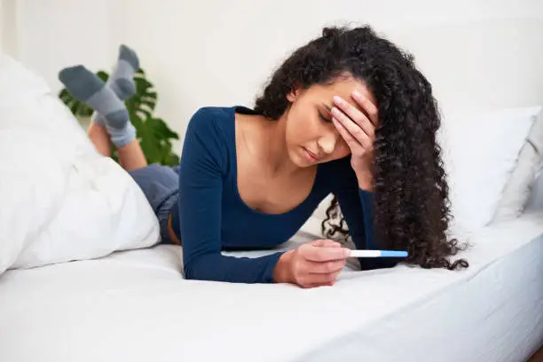 A young multi-ethnic woman lays in bed looking at unwanted pregnancy test result. High quality photo