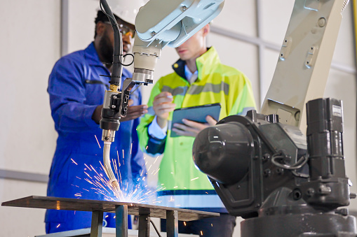 Close up an automatic welding torch with a multiracial Engineer colleague discussing the Robot Development Plant, smart factory, and Industry Engineering Intelligence Innovation Technology concept