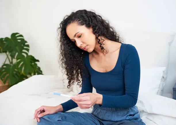 A young multi-ethnic woman sits holding pregnancy test waiting for result. High quality photo