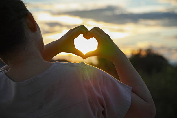 istock Heart shape with female hands over sunset sky background 1423993073