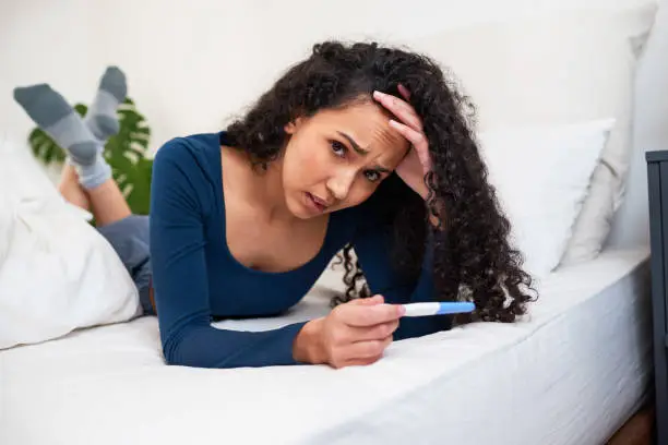 A young multi-ethnic woman lays in bed looking at unwanted pregnancy test result. High quality photo