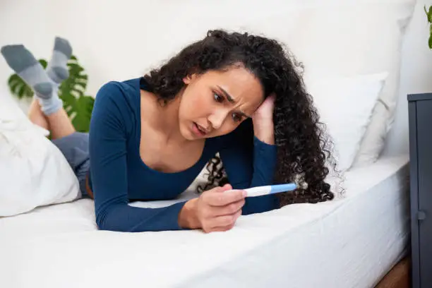 A young multi-ethnic woman lays in bed looking at unwanted pregnancy test result. High quality photo