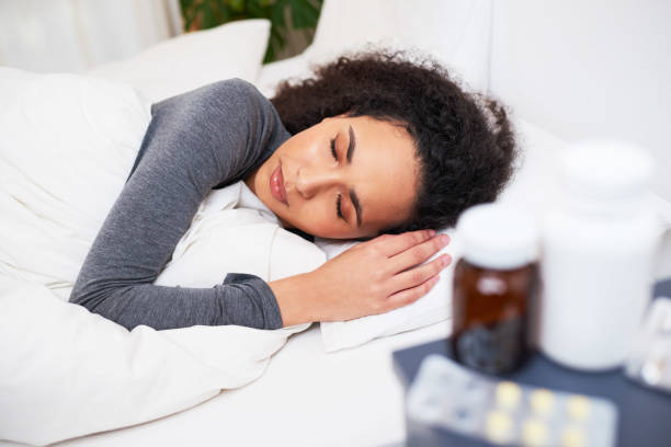 A young multi-ethnic woman sleeps in bed recovering from flu with medication stock photo