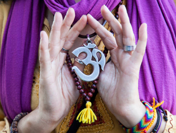 Om Close-up of a om symbol pendant in the hands of a woman with purple shawl om symbol stock pictures, royalty-free photos & images