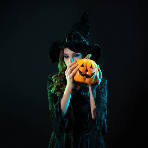 istock tricky beautiful witch in a pointed hat Holding a pumpkin with a laughing face, 1424001623