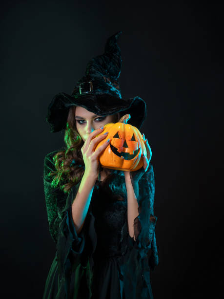 istock tricky beautiful witch in a pointed hat Holding a pumpkin with a laughing face, 1424001629