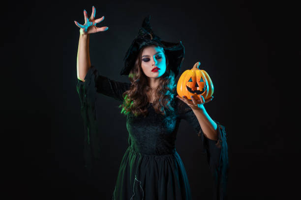 istock beautiful witch with a hat make spell over jack-o-lantern pumpkin. 1424001632