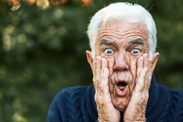 älterer mann mit weißen haaren sieht schockiert, verängstigt und entsetzt mit den händen im gesicht und offenem mund aus - fear terrified shock humor stock-fotos und bilder