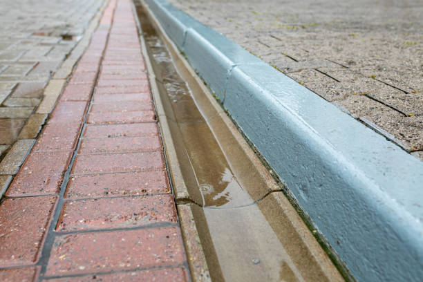 istock Rainwater runoff during rain. Concrete gutter for rainwater drainage between the sidewalk and the roadway. 1424008466