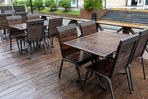 Empty wet wooden tables and chairs in outdoor cafeteria during rain. Street city life in rain