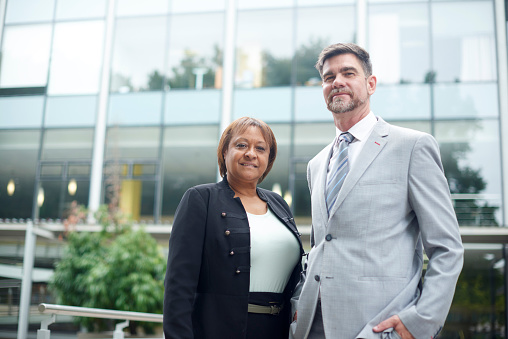 Portrait, businessman and woman in the city standing outside of their office building or company. Diverse business people or partners and coworkers in the street or urban corporate workplace.