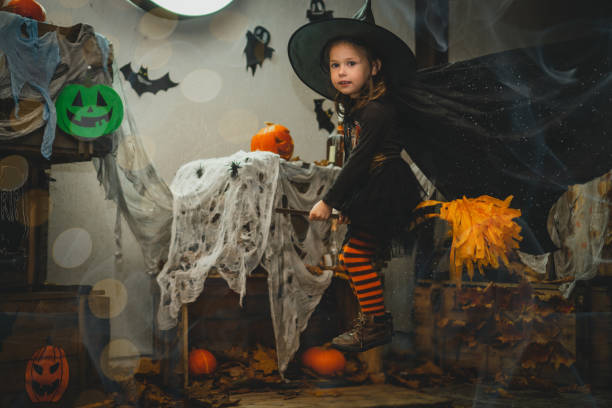 little girl 3-4 years old in witch costume and striped stockings flies on broom in halloween decorated yard - child caucasian little girls 3 4 years imagens e fotografias de stock