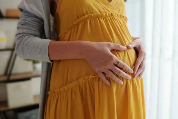 Pregnant woman making heart gesture when keeping hands on belly