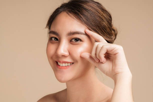 Closeup photo of a smiling brunette asian woman touching her eyes with natural makeup stock photo