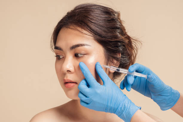 Closeup face young asian woman is getting filler under her eye for anti age wrinkle by a beautician with a syringe in hands. stock photo