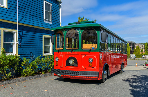 Bar Harbor, Maine, USA - October 2, 2021: A sunny Autumn morning view of a bright red-green local tour bus parking in an alleyway at center of the resort town.