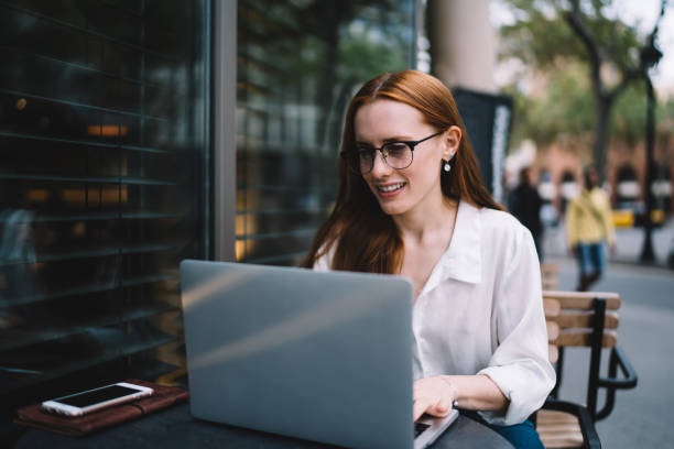 istock Smiling woman using laptop in street cafe 1424013340