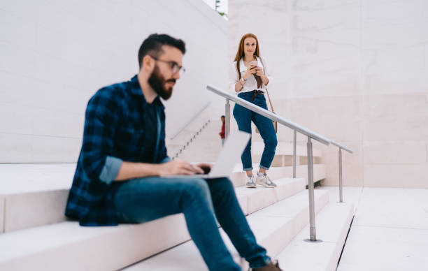 istock Young woman using smartphone while standing on stairs in modern university building 1424013796