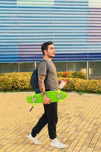 Young man walking through the city on his skateboard while drinking coffee.