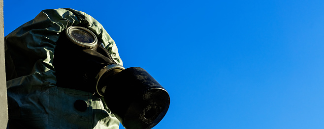 Side close view of person wearing gas mask and protective chemical suit against blue sky with copy space outdoor