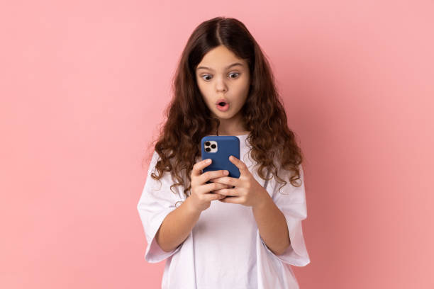 shocked astonished little girl reading shocking post on social network using cell phone. - surprise child little girls shock imagens e fotografias de stock