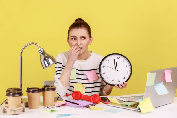 istock Woman worker biting nails holding big wall clock, sitting at workplace all covered with sticky notes 1424033217