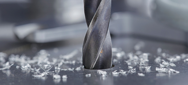 metal drill bit make holes in steel billet on industrial drilling machine with shavings. Metal work industry. multi cutting tool and end mill.