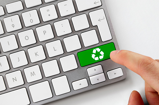 Human finger pushes green recycle button on computer keyboard