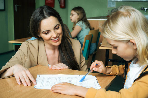 istock Elementary school teacher explaining to schoolboy at desk in lesson 1424043496