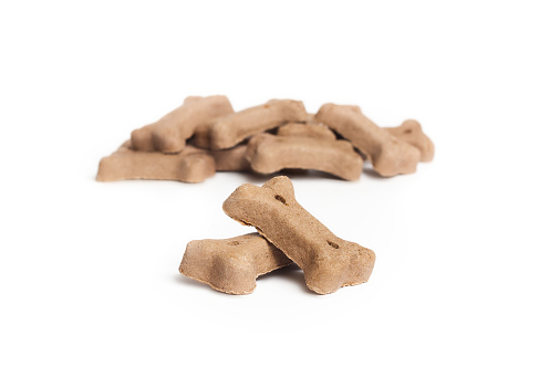 Isolated chewing bones in a pile. Small brown or beige pet food for snacking, training, enjoyment or dental hygiene. Selective focus. White background.