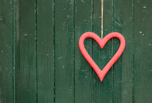 red heart shape hanging in front of a textured green door, close up, love concept