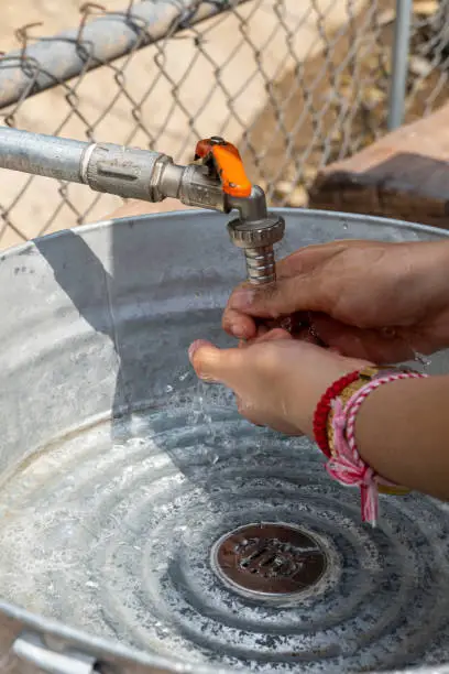 woman washing her hands outside, in a makeshift sink made of metal and pipes. mexico, guadalajara concept of health and cleanliness, use of liquid soap