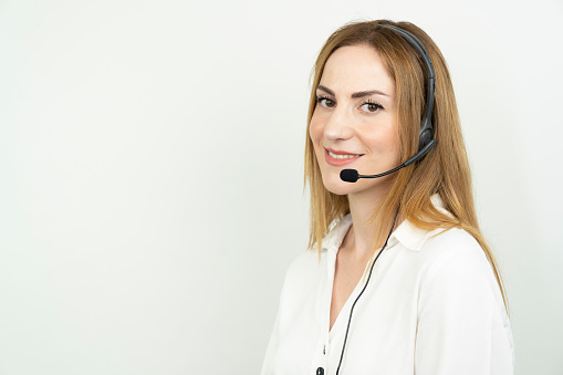 Photo of beautiful young call center operator standing near white background. Woman with headphones smiling