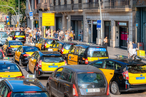 Barcelona, Spain - August 29, 2022: People walking on the sidewalk of a street in a commercial district. There is a heavy traffic jam on the road.