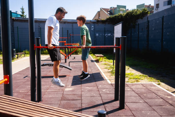 Father exercising with his son on  a dip station at outdoor gym stock photo