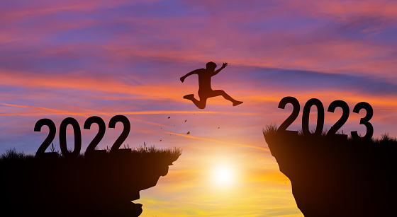 Welcome merry Christmas and Happy new year in 2023. Man jumping across the gap from 2022 to 2023 cliff with Sunset and Twilight Sky background.