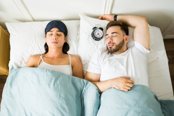 pareja agotada durmiendo en la cama con un despertador - dormir fotografías e imágenes de stock