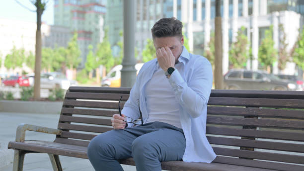istock Man with Headache Sitting Outdoor on Bench 1424109665