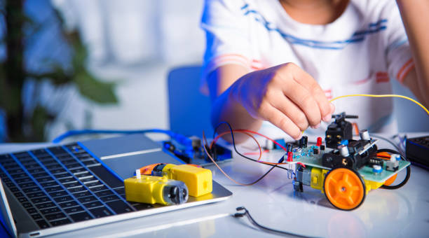 istock Asian kid boy plugging energy and signal cable to sensor chip with open-source hardware and software robot car 1424118395